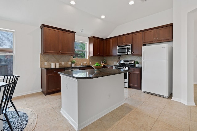 kitchen with stainless steel appliances, a kitchen island, light tile patterned floors, decorative backsplash, and vaulted ceiling