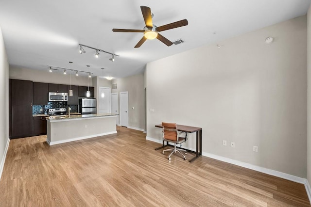 kitchen with a kitchen island with sink, light wood-style flooring, stainless steel appliances, visible vents, and decorative backsplash