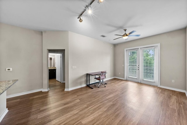 unfurnished living room with a ceiling fan, track lighting, baseboards, and wood finished floors