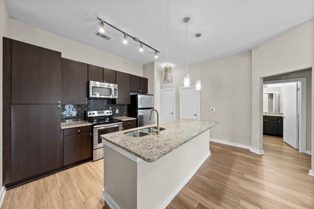 kitchen featuring sink, appliances with stainless steel finishes, dark brown cabinetry, an island with sink, and decorative light fixtures