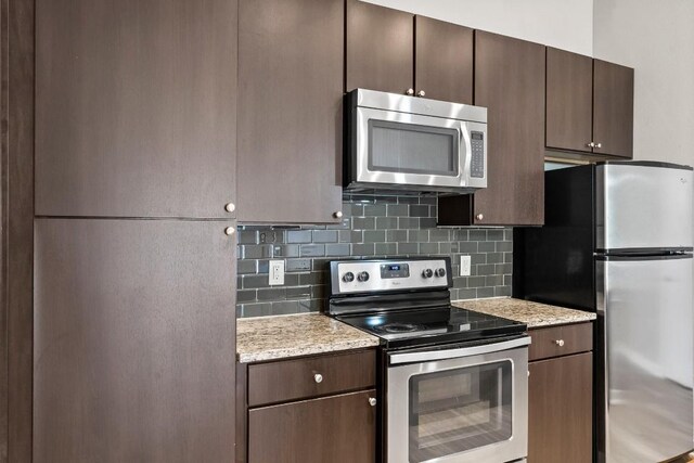 kitchen featuring stainless steel appliances, tasteful backsplash, light stone counters, and dark brown cabinets