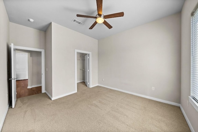 unfurnished bedroom with light colored carpet, a walk in closet, visible vents, and baseboards