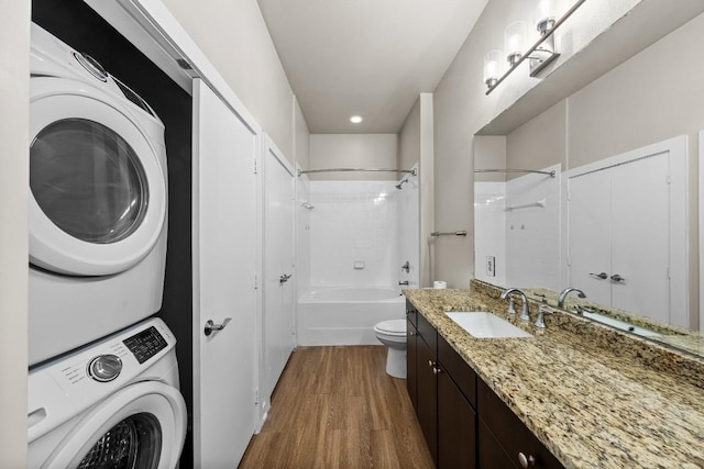 bathroom with toilet, shower / tub combination, stacked washer / drying machine, wood finished floors, and vanity