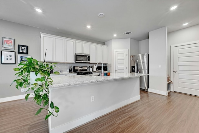 kitchen with white cabinets, light wood-type flooring, stainless steel appliances, and backsplash