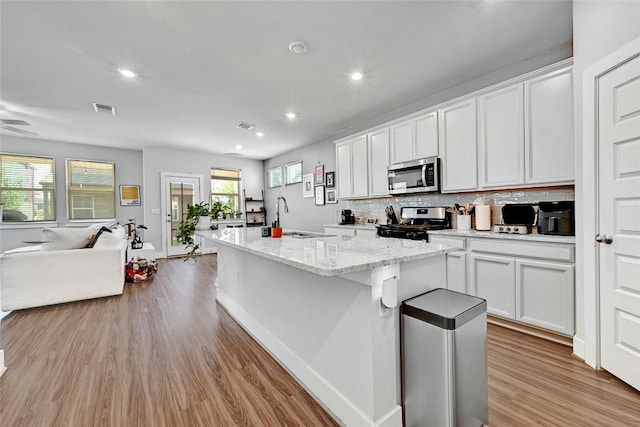 kitchen featuring light hardwood / wood-style flooring, white cabinetry, a center island with sink, and appliances with stainless steel finishes