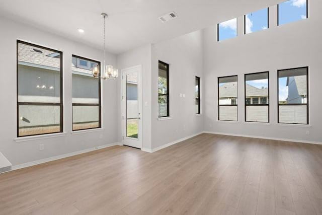 spare room featuring a chandelier, light hardwood / wood-style floors, and a high ceiling