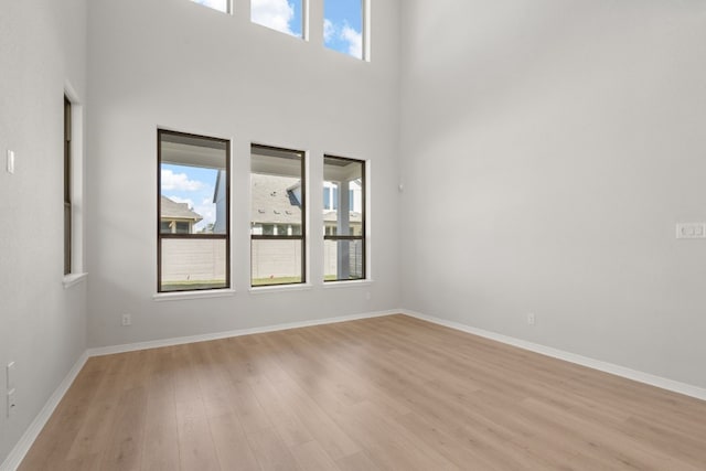 unfurnished room featuring light wood-type flooring and a towering ceiling