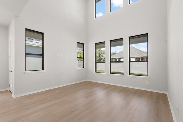 empty room with a towering ceiling, light hardwood / wood-style floors, and a wealth of natural light