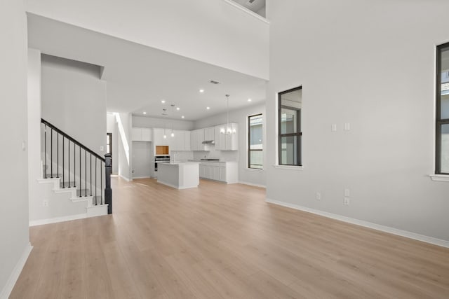 unfurnished living room featuring a notable chandelier, light wood-type flooring, and a high ceiling