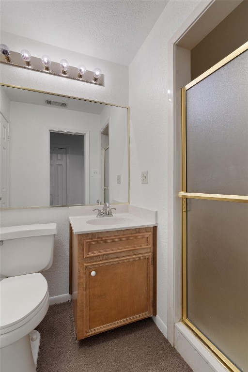 bathroom with a textured ceiling, toilet, vanity, and an enclosed shower