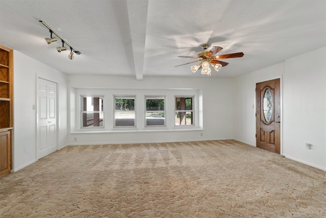 unfurnished living room with beamed ceiling, track lighting, light colored carpet, a textured ceiling, and ceiling fan