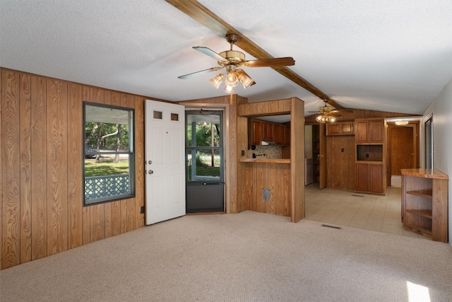 unfurnished living room featuring vaulted ceiling with beams, a textured ceiling, wood walls, light carpet, and ceiling fan