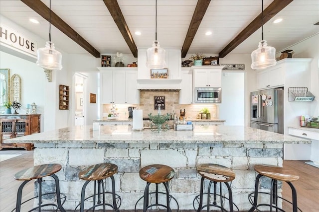 kitchen featuring light stone countertops, stainless steel appliances, pendant lighting, beam ceiling, and white cabinetry