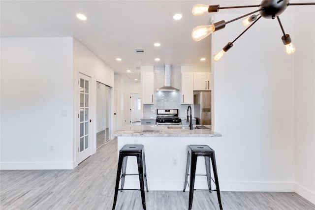 314 Saxon Ln, Austin, TX 78741 - kitchen with stainless steel appliances, wall chimney exhaust hood, white cabinets, light wood-style flooring, and a kitchen bar