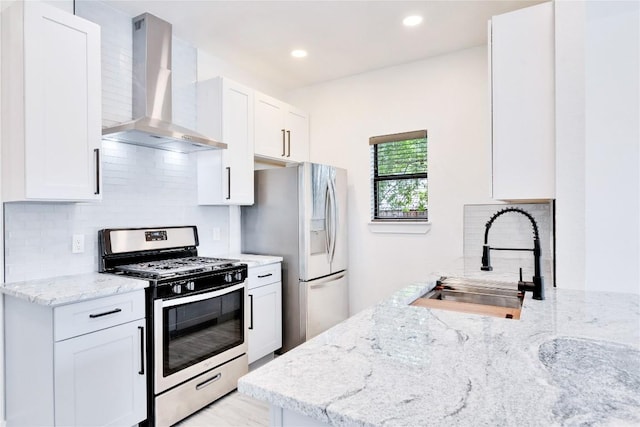 kitchen featuring decorative backsplash, wall chimney exhaust hood, light stone counters, appliances with stainless steel finishes, and a sink