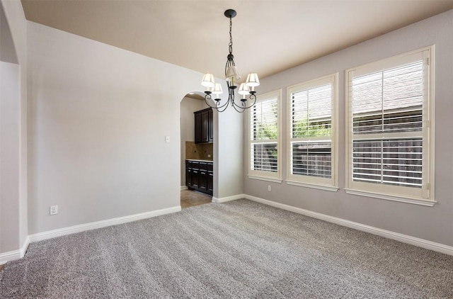 carpeted spare room with an inviting chandelier