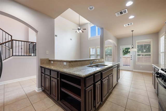 kitchen with sink, range, light tile patterned floors, light stone counters, and dark brown cabinetry