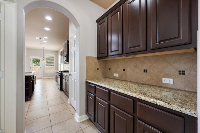 kitchen with light tile patterned floors, hanging light fixtures, dark brown cabinets, light stone countertops, and range with gas cooktop