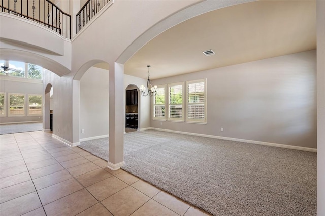 unfurnished living room with ceiling fan with notable chandelier, light colored carpet, and a high ceiling