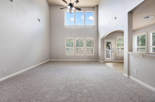 unfurnished living room with ceiling fan, light carpet, and a high ceiling