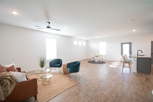 living room featuring light wood-type flooring, ceiling fan, and sink