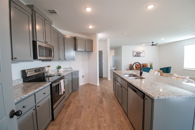 kitchen featuring light stone counters, light hardwood / wood-style floors, sink, a center island with sink, and appliances with stainless steel finishes