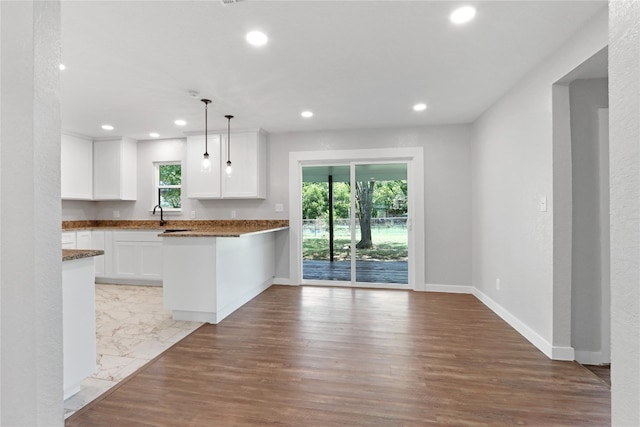 kitchen with kitchen peninsula, hanging light fixtures, light wood-type flooring, dark stone countertops, and white cabinetry