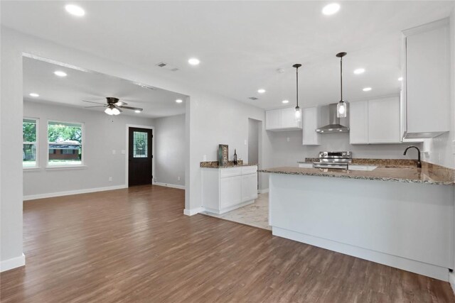 kitchen with wall chimney range hood, a peninsula, dark stone counters, and electric range