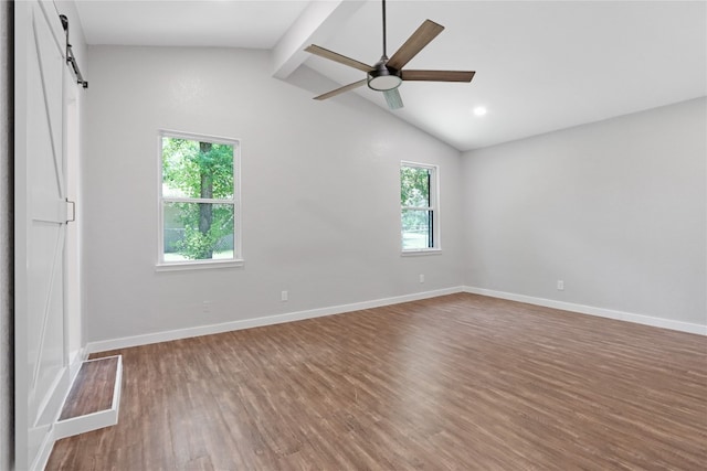 spare room with lofted ceiling with beams, ceiling fan, hardwood / wood-style flooring, and a barn door