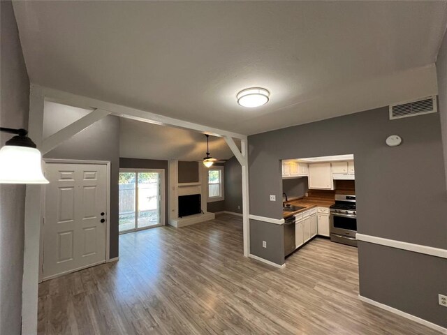 kitchen with wood-type flooring, stainless steel appliances, hanging light fixtures, white cabinets, and vaulted ceiling