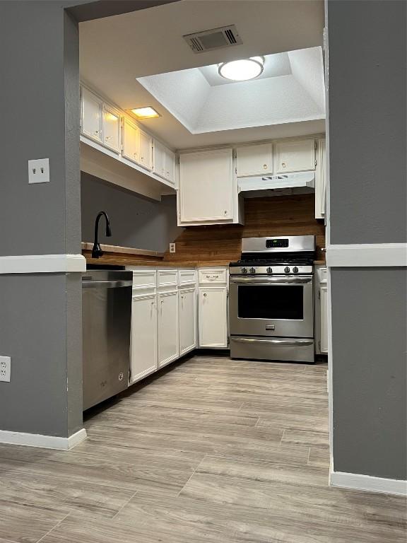 kitchen with white cabinets, a raised ceiling, light hardwood / wood-style flooring, and appliances with stainless steel finishes