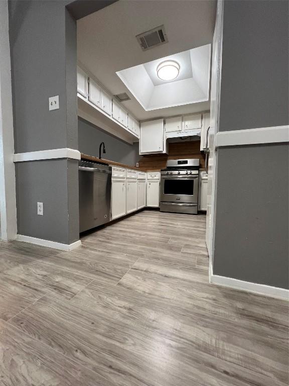 kitchen with appliances with stainless steel finishes, white cabinetry, light wood-type flooring, and a tray ceiling