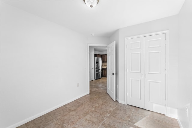 unfurnished bedroom featuring stainless steel fridge, light tile patterned floors, and a closet