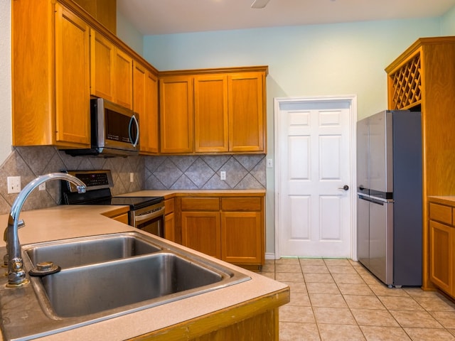 kitchen with appliances with stainless steel finishes, light tile patterned floors, decorative backsplash, and sink