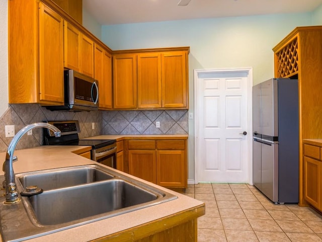 kitchen featuring light tile patterned flooring, appliances with stainless steel finishes, a sink, brown cabinetry, and tasteful backsplash