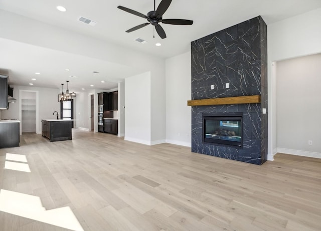 unfurnished living room with a high end fireplace, sink, light wood-type flooring, and ceiling fan with notable chandelier