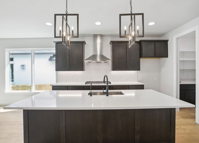 151 William Hersee Dr, Bastrop, TX 78602 - kitchen with wall chimney exhaust hood, a sink, light countertops, a kitchen island with sink, and light wood-style floors
