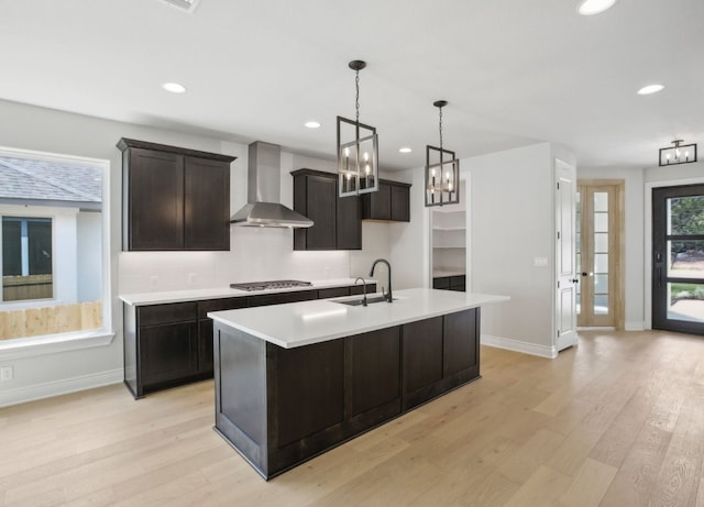 kitchen with light hardwood / wood-style floors, a center island with sink, stainless steel gas stovetop, wall chimney exhaust hood, and sink