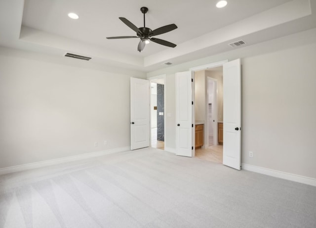 unfurnished bedroom featuring light carpet, ceiling fan, and a raised ceiling