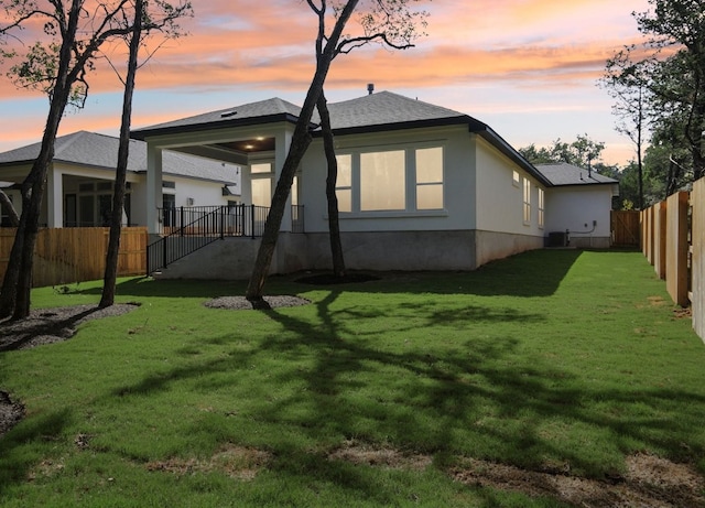 back house at dusk with central AC unit and a lawn