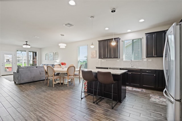 kitchen featuring light hardwood / wood-style flooring, stainless steel fridge, pendant lighting, a breakfast bar area, and a kitchen island