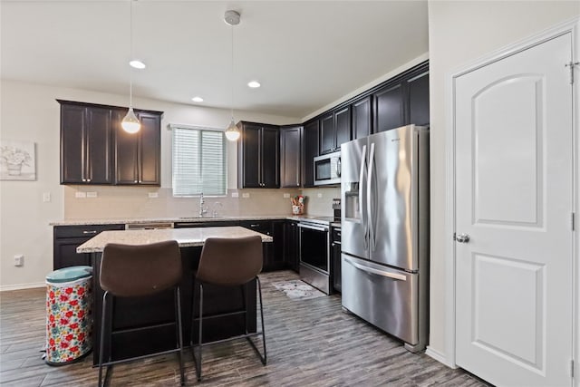 kitchen featuring a kitchen breakfast bar, stainless steel appliances, decorative light fixtures, hardwood / wood-style floors, and a center island