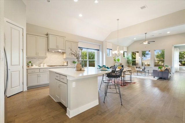 kitchen with backsplash, light hardwood / wood-style flooring, lofted ceiling, ceiling fan with notable chandelier, and pendant lighting