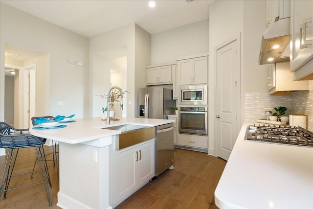 kitchen featuring custom range hood, hardwood / wood-style flooring, decorative backsplash, a kitchen island with sink, and stainless steel appliances