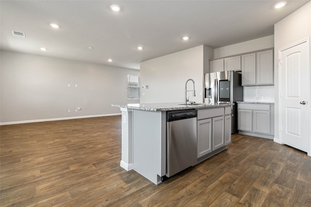 kitchen featuring stainless steel appliances, gray cabinetry, a center island with sink, and dark wood-type flooring