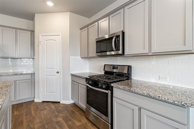 kitchen with tasteful backsplash, dark wood-type flooring, light stone counters, gray cabinets, and appliances with stainless steel finishes