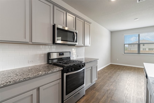 kitchen with stainless steel appliances, gray cabinetry, decorative backsplash, light stone countertops, and dark hardwood / wood-style flooring