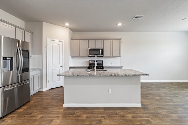 kitchen featuring dark wood-type flooring, light stone countertops, a center island with sink, appliances with stainless steel finishes, and gray cabinetry