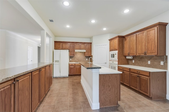 kitchen featuring white appliances, a center island with sink, sink, backsplash, and light tile patterned floors