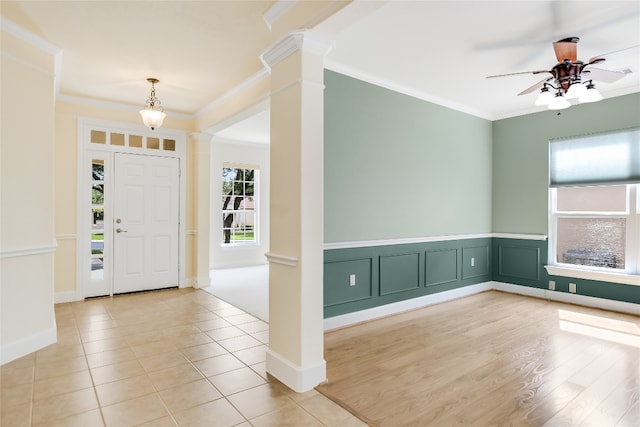 foyer entrance featuring light wood-type flooring, crown molding, ornate columns, and ceiling fan